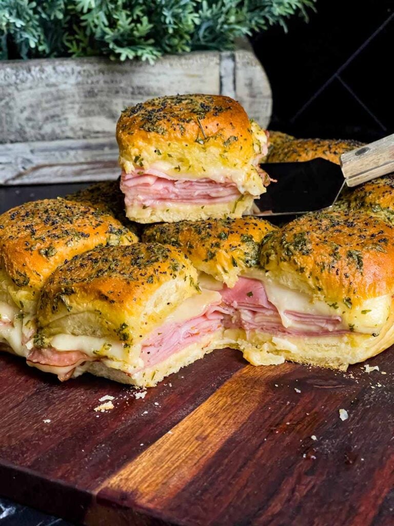 Ham and swiss cheese sliders on a wooden cutting board.