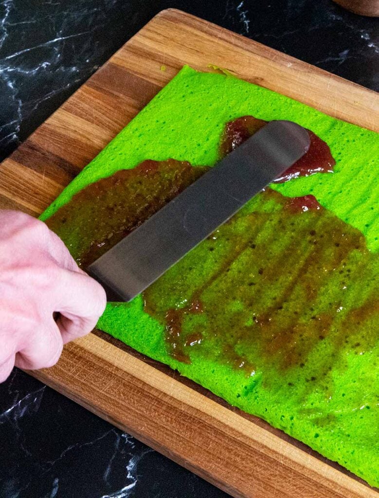 Raspberry jam being spread on the green cookie layer.