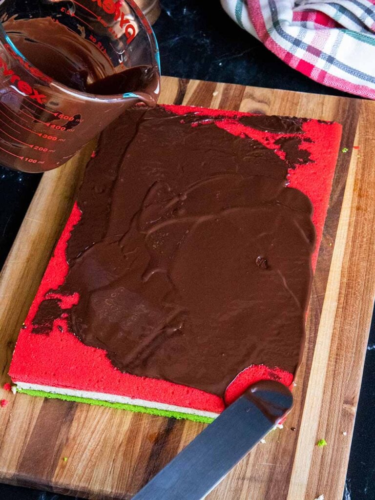 Chocolate being spread over the red cookie layer.