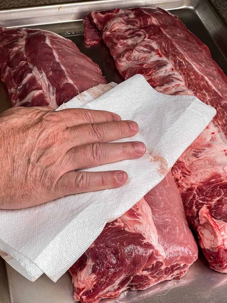 Drying baby back ribs off with a paper towel.