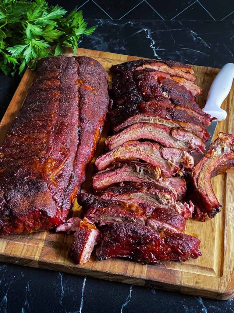 Two racks of baby back ribs, one of which is cut up on a wooden cutting board.