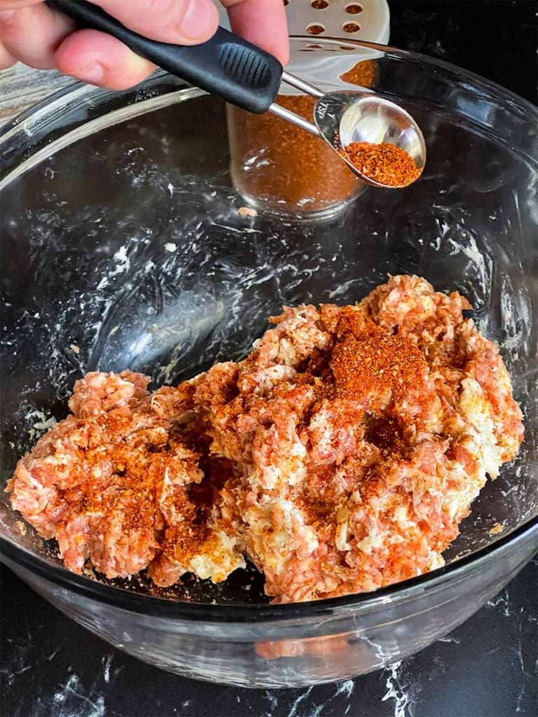 Adding barbecue rub to the sausage mixture in a glass bowl for the smoked shotgun shells.