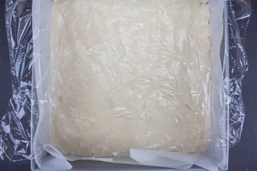 Dough pressed into a baking pan with plastic wrap.