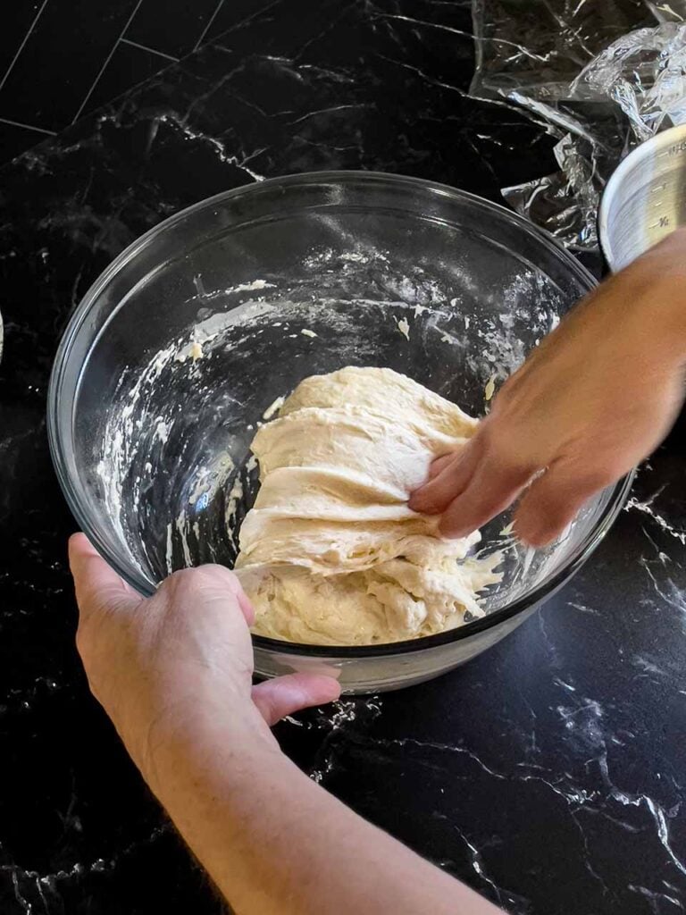 Stretching and folding the focaccia bread dough in a glass bowl.