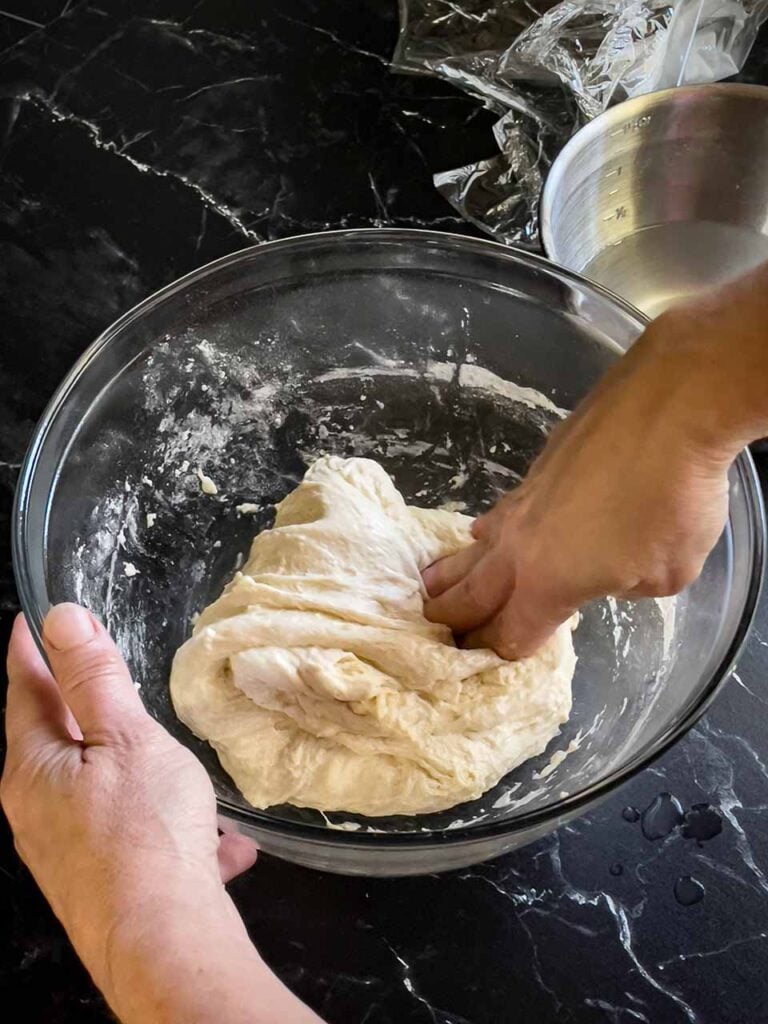 Stretching and folding the focaccia dough a second time in a glass bowl.