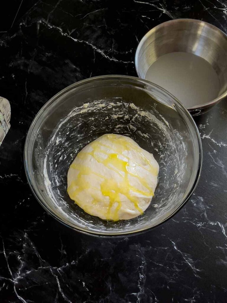 Focaccia dough, topped with olive oil, in a glass bowl.