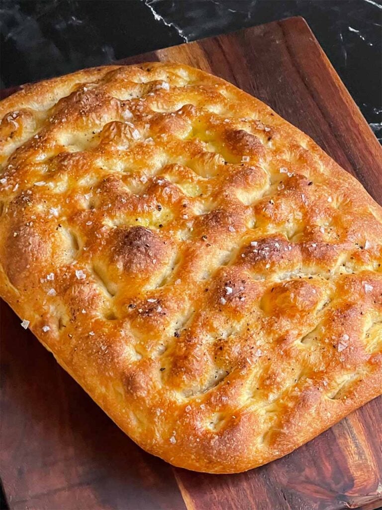 focaccia bread right out of the oven on a wooden cutting board.