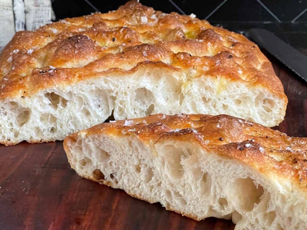 Overnight focaccia bread cut in half on a wooden cutting board.