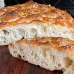 Overnight focaccia bread cut in half on a wooden cutting board.