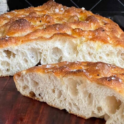 Overnight focaccia bread cut in half on a wooden cutting board.