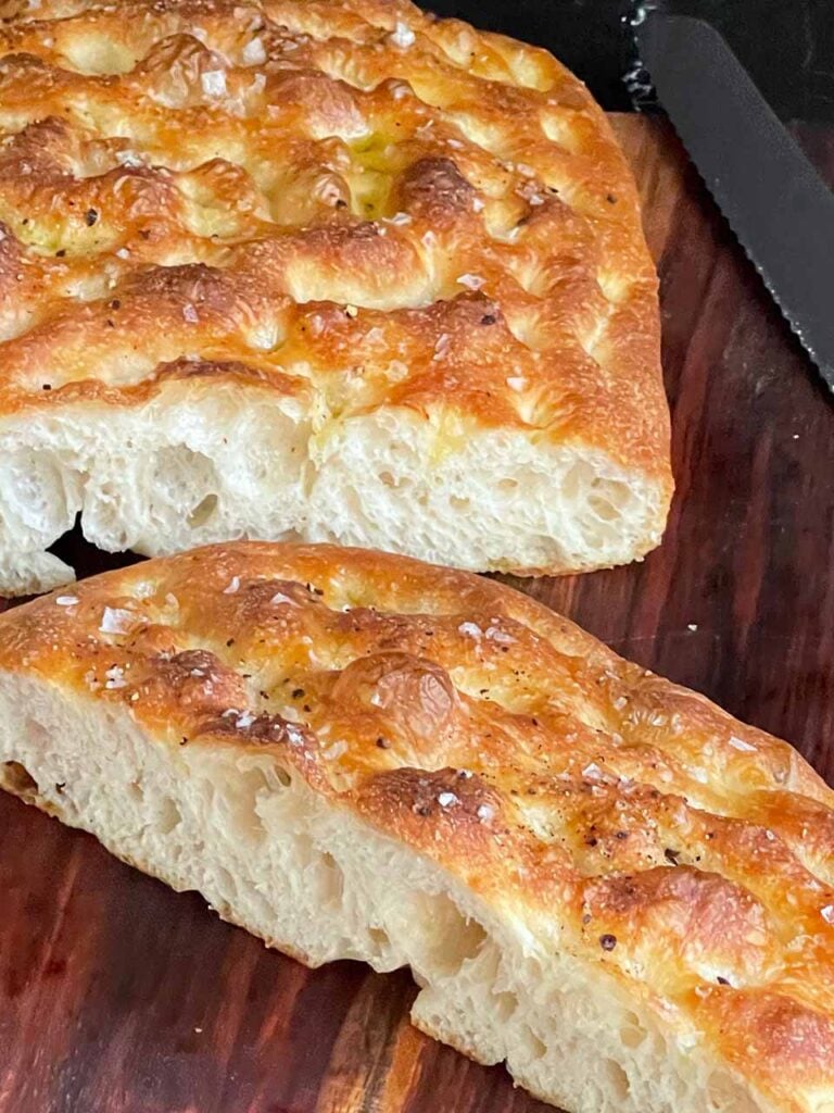 Fresh baked overnight focaccia cut in half on a wooden cutting board.