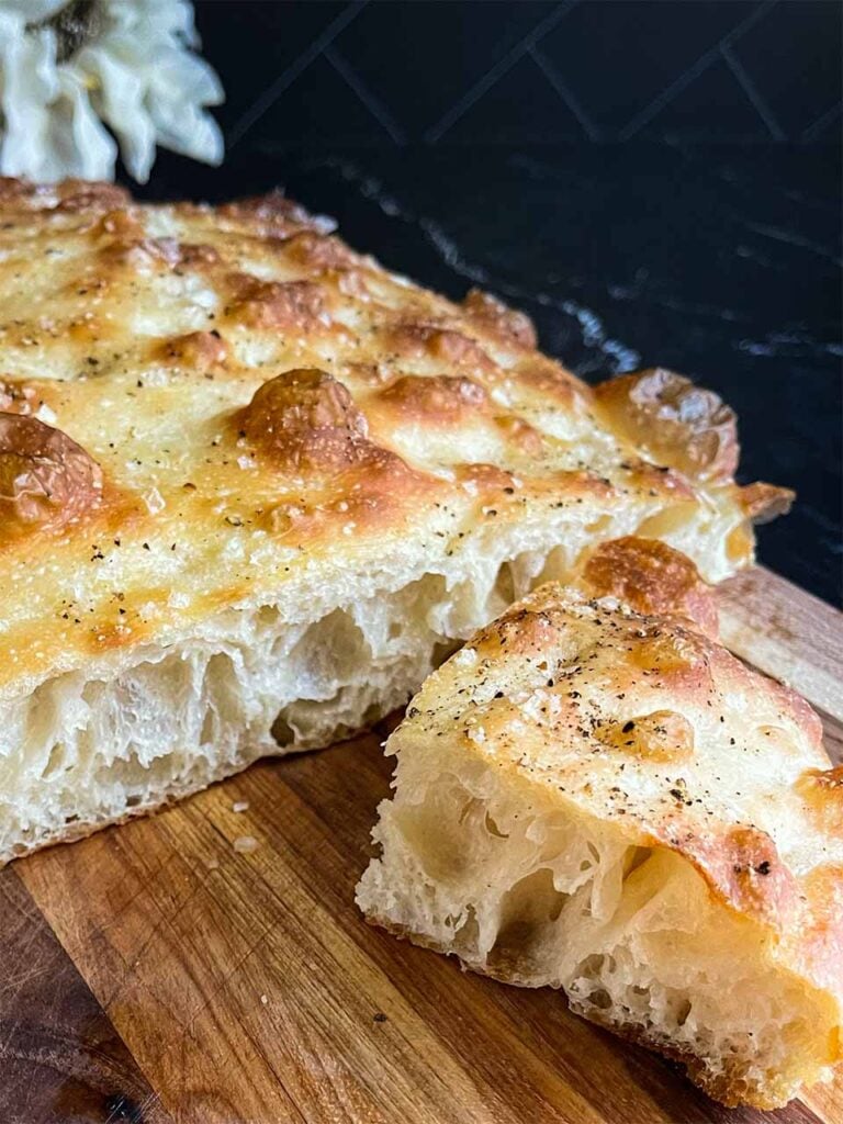Baked overnight focaccia bread, cut, on a wooden cutting board.