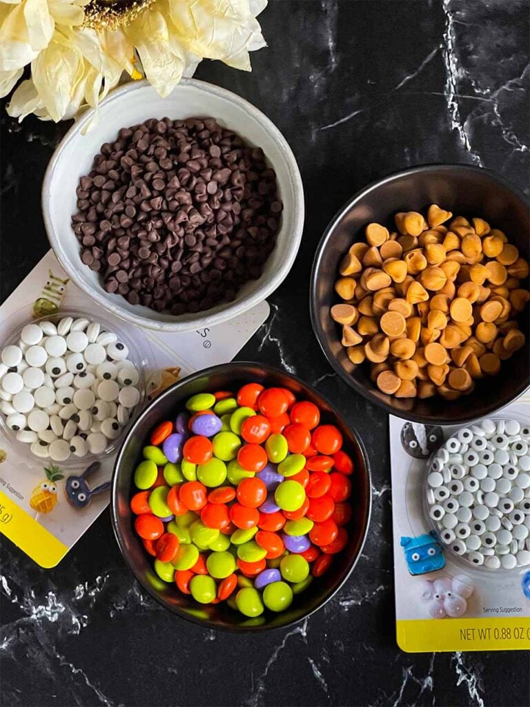 M and M's, mini semi-sweet chocolate chips, butterscotch chips, and candy eyes on a black marble counter top.