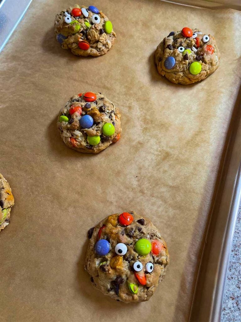 Baked Halloween monster cookies with candy eyes on a parchment lined baking sheet.