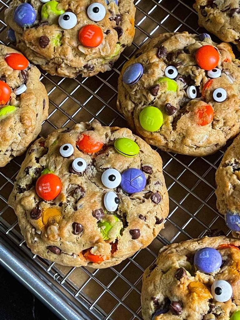 Halloween monster cookies with eyes on a wire rack in a baking sheet.