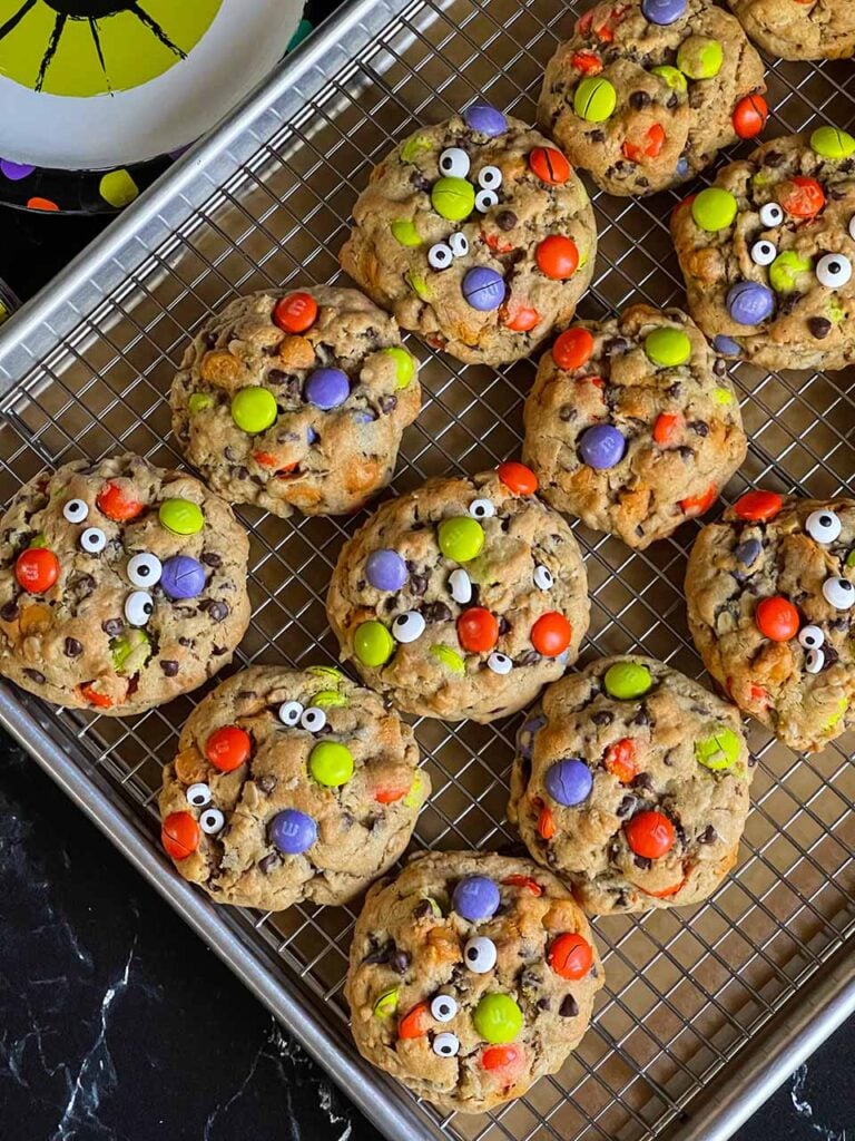 Halloween monster cookies with eyes on a wire rack in a baking sheet.