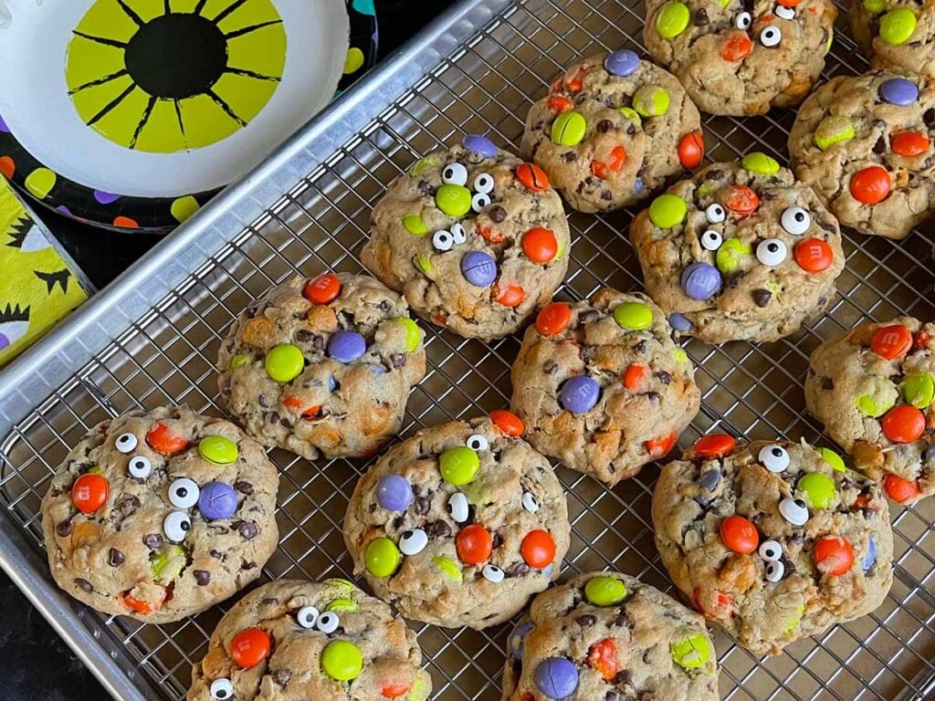 Halloween monster cookies on a wire rack in a baking sheet.