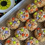 Halloween monster cookies on a wire rack in a baking sheet.