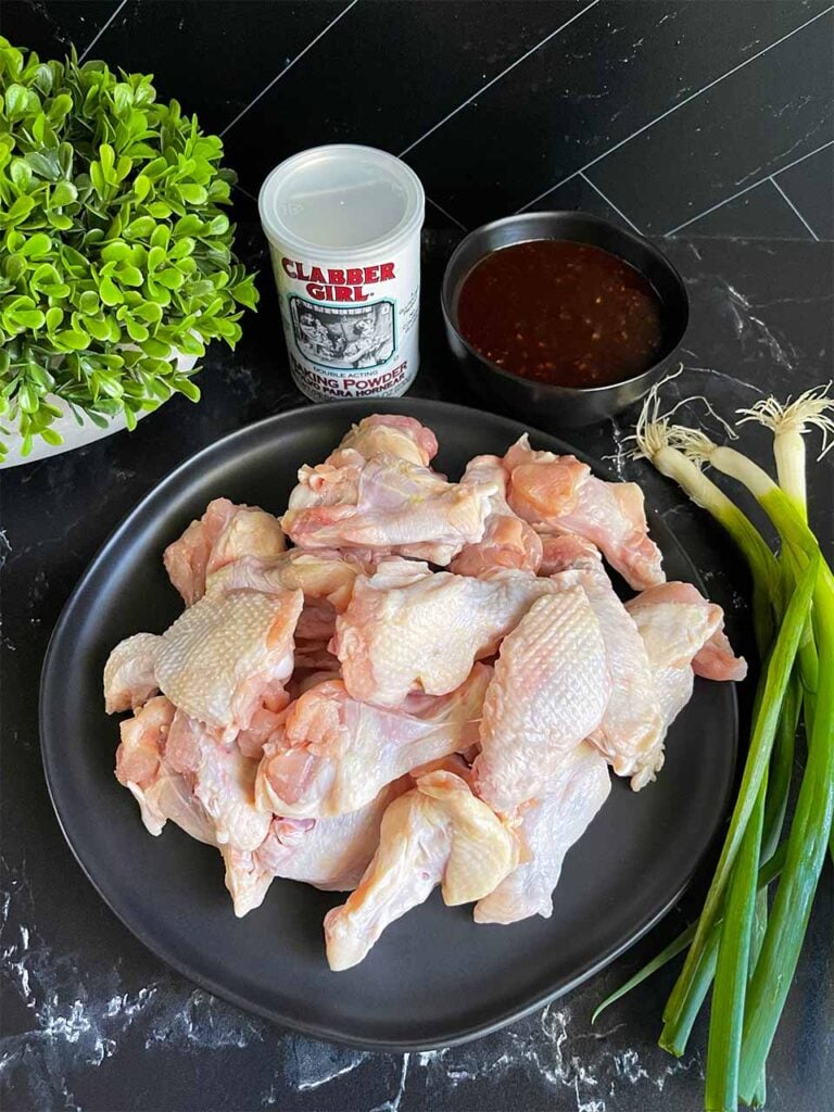 Raw chicken wings on a black plate with green onions off to the side.