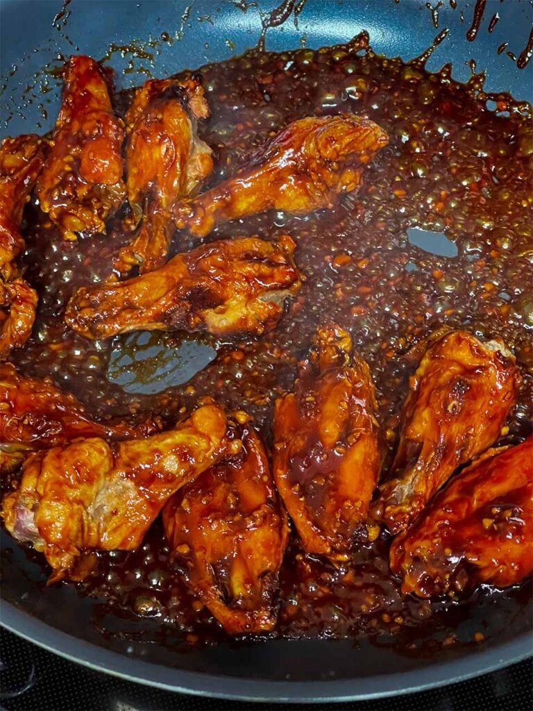 Wings in a skillet being coated by the asian dipping sauce.