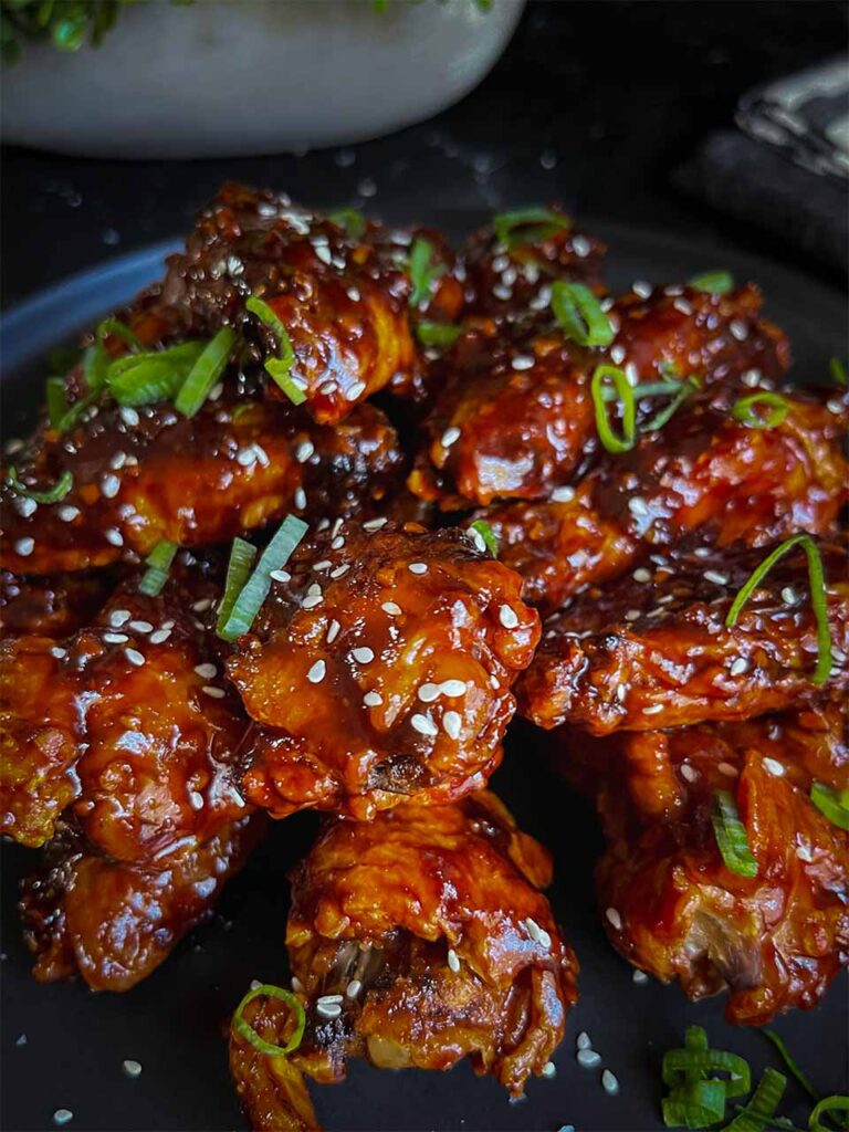 A plate of Asian chicken wings on a black plate garnished with green onions and sesame seeds.