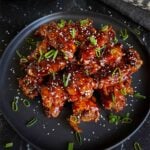 A plate of Asian chicken wings garnished with green onions and sesame seeds.