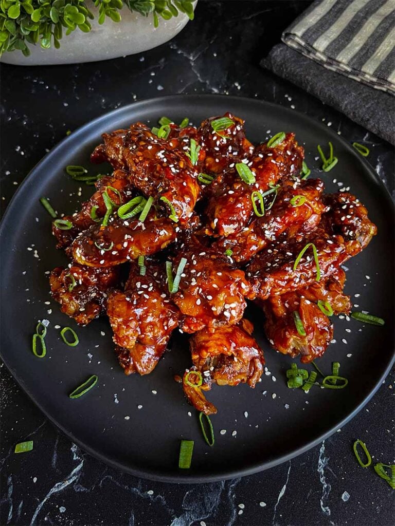 A plate of Asian chicken wings garnished with green onions and sesame seeds.