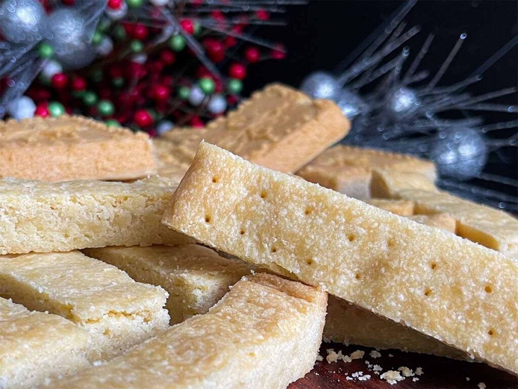 Classic shortbread cookies in stick shape and shortbread pan shape on a wooden cutting board.