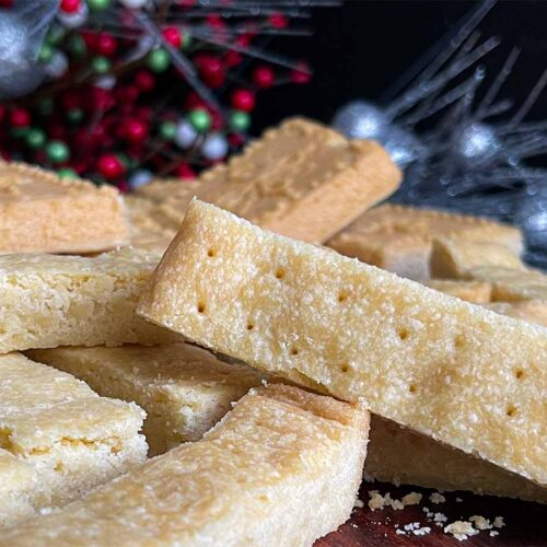 Classic shortbread cookies in stick shape and shortbread pan shape on a wooden cutting board.