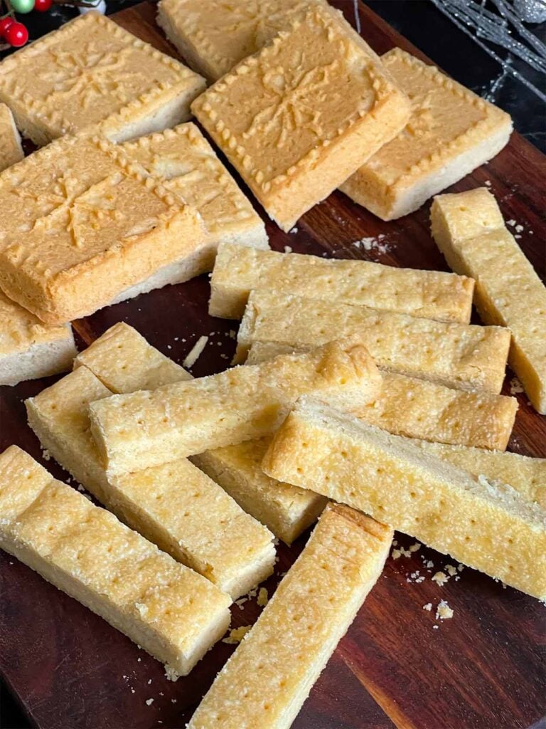 Classic shortbread cookies in stick shape and shortbread pan shape on a wooden cutting board.