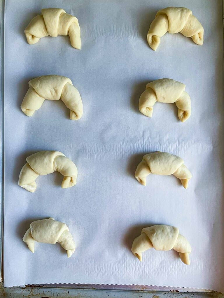 Unbaked crescent rolls on a parchment paper lined baking sheet.