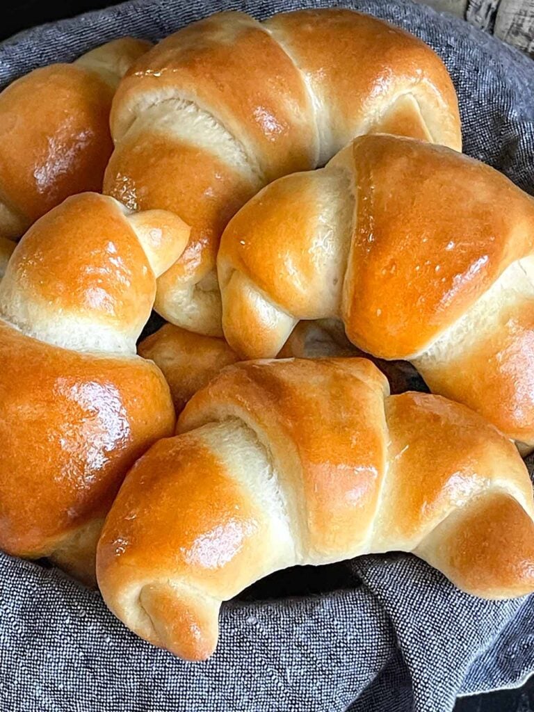 Crescent rolls in a bread basket lined with gray towel.