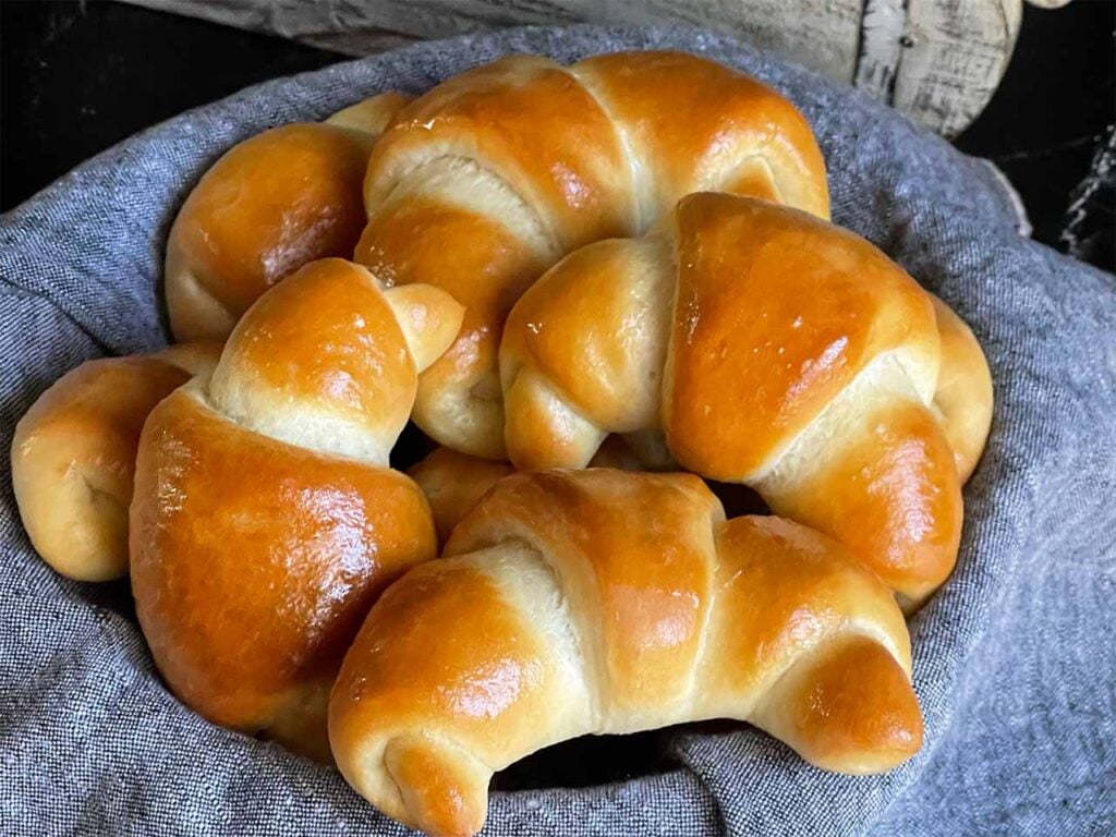 Crescent rolls in a bread basket lined with gray towel.
