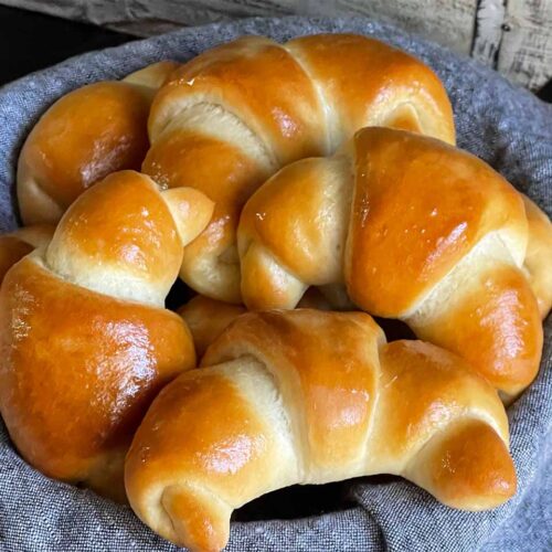 Crescent rolls in a bread basket lined with gray towel.