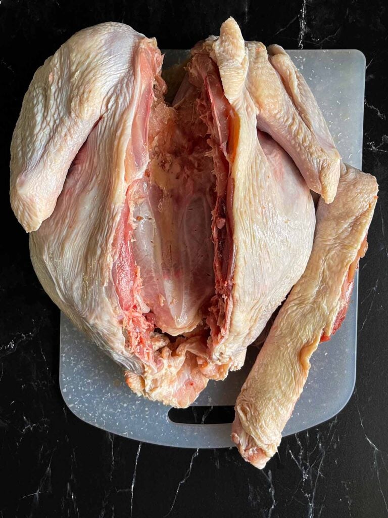 A turkey with its backbone removed on a white cutting board.