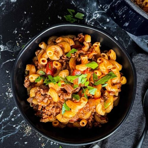 A bowl of goulash in a dark bowl.