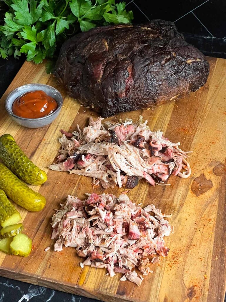 A cutting board with a whole smoked pork butt, shredded smoked pork butt, and chopped smoked pork butt.