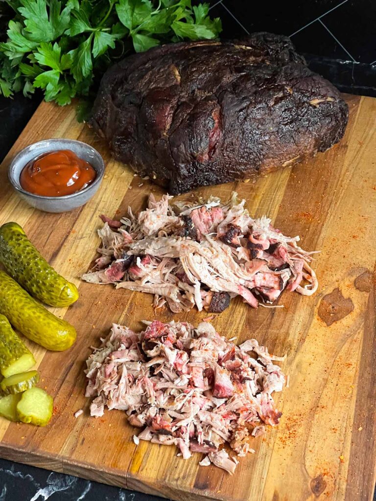 A cutting board with a whole smoked pork butt, shredded smoked pork butt, and chopped smoked pork butt.