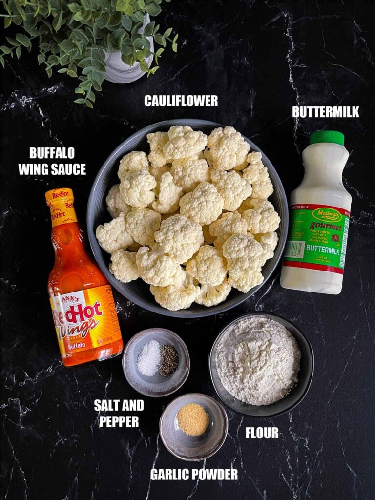 Ingredients for baked buffalo cauliflower bites on a dark surface.