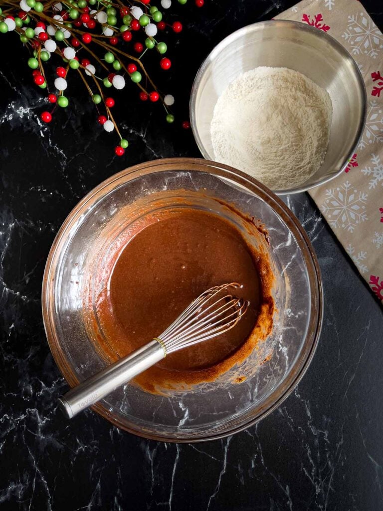 The wet ingredients for chocolate crinkle cookies in a glass bowl with the dry ingredients in a metal bowl next to it.