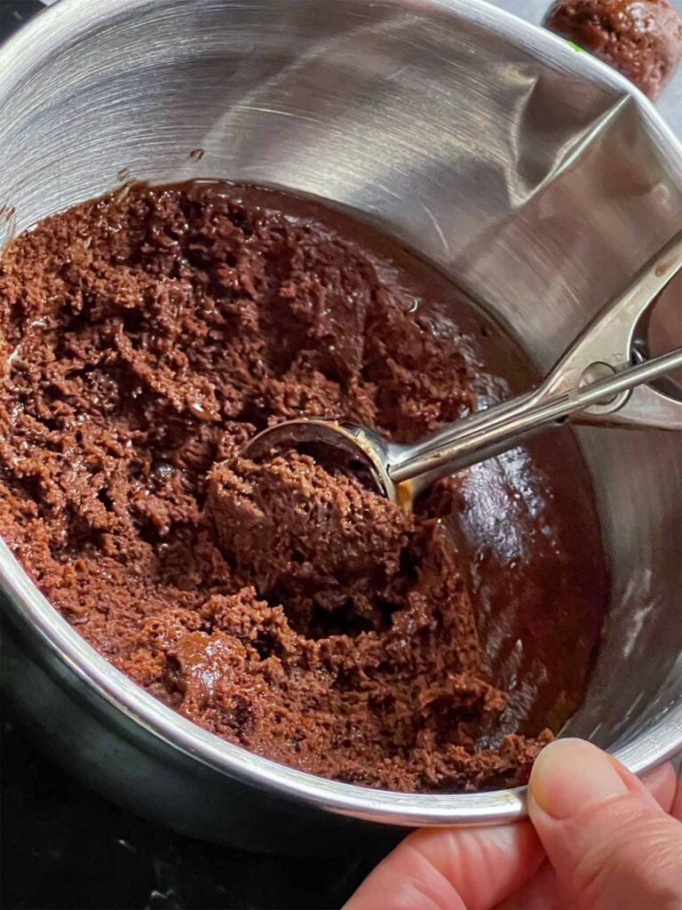 Chilled chocolate crinkle cookie dough in a metal bowl with a cookie scoop being used to form balls,