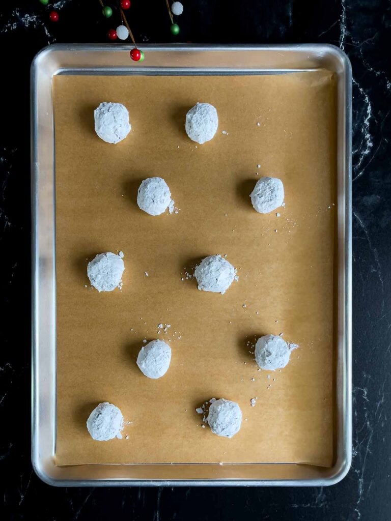 Chocolate crinkle cookie dough balls coated in sugar on a parchment paper lined baking sheet.