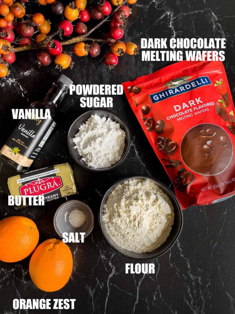 Ingredients needed to make chocolate orange shortbread cookies on a dark surface.