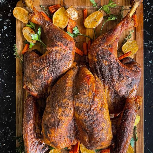 Dry brined spatchcock turkey with roasted vegetables on a wooden cutting board.
