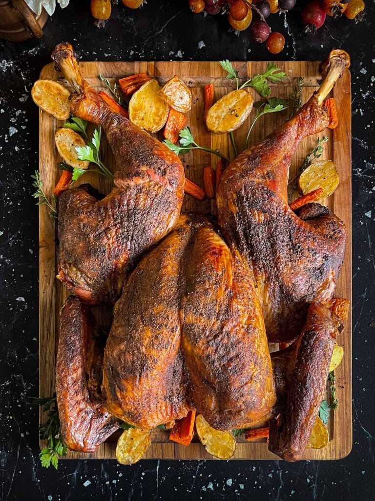 Dry brined spatchcock turkey with roasted vegetables on a wooden cutting board.