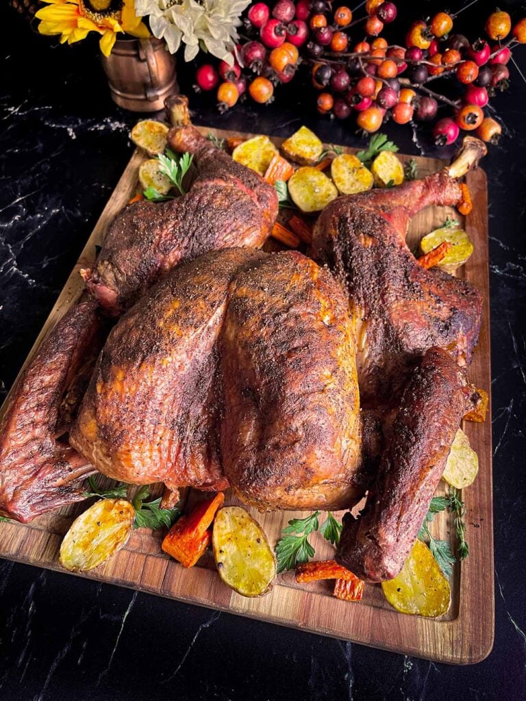 Dry brined spatchcock turkey with roasted vegetables on a wooden cutting board.