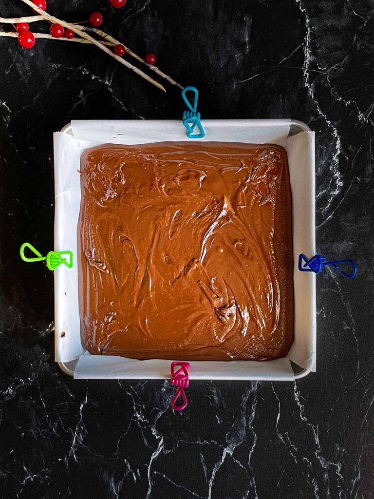 Dark chocolate fudge poured into a baking pan lined with parchment paper.