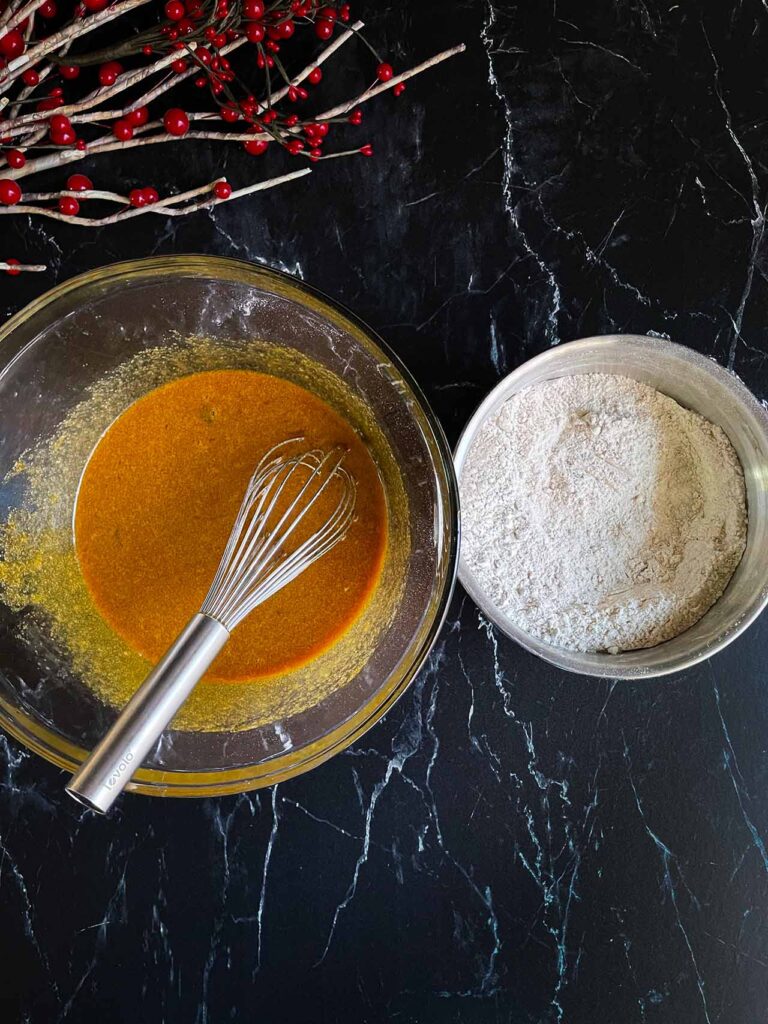 Wet ingredients mixed in a glass bowl and dry ingredients mixed in a metal bowl on a dark background.