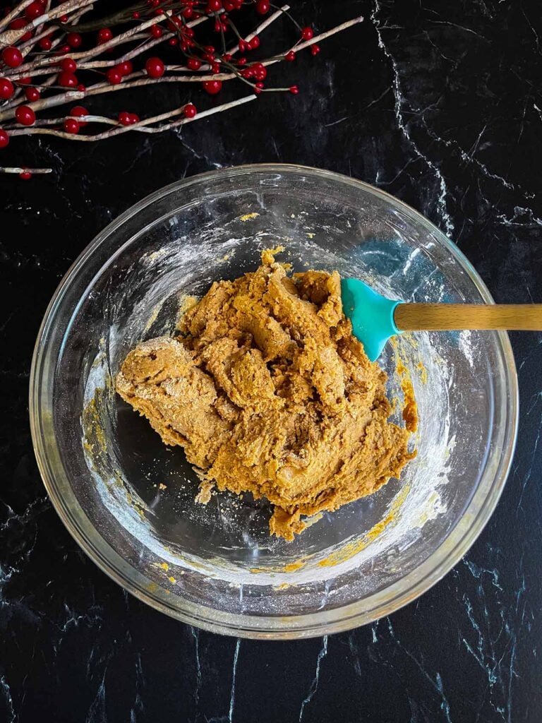 Gingerbread biscotti dough in a glass mixing bowl on a dark background.