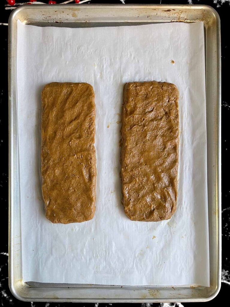 Gingerbread biscotti dough logs on a parchment paper lined baking sheet.